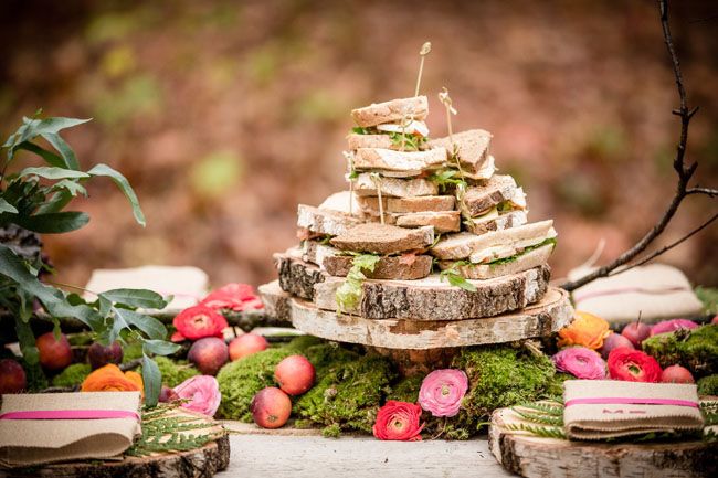 A woodland food display    a moss runner with apples and bright blooms, wood slice stands and chargers look super cool