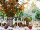 a boho woodland wedding tablescape with fall leaves, greenery and berries, fruits, amber glasses and colorful plates