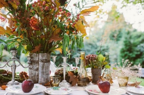 a boho woodland wedding tablescape with fall leaves, greenery and berries, fruits, amber glasses and colorful plates