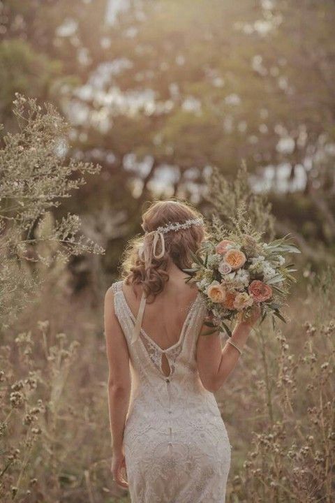 a boho woodland summer bride wearing a beautiful lace wedding dress with a cutout back, a lace headpiece and carrying a lovely neutral bouquet
