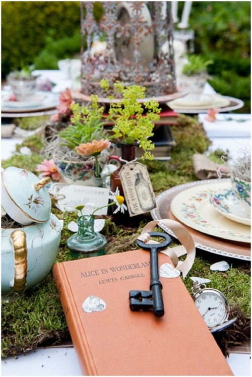 an enchanted forest wedding tablescape with a moss runner, greenery and blooms in vases, teapots and sugar pots with vintage keys