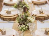 a simple woodland wedding tablescape with a burlap runner, wood slice placemats, blooms and greenery and tree stumps for holding cards