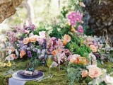 a romantic enchanted forest wedding tablescape covered with moss and lush blooms and greenery plus purple glass plates and a neutral napkin