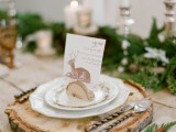 a cozy place setting with a wood slice as a placemat, plates, a card with a deer held by a tree slice