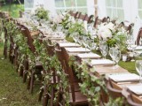 a woodland wedding tablescape with a moss runner, greenery and white blooms in vases and chairs decorated with greenery