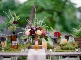 a woodland wedding tablescape with a moss runner, bold blooms and greenery and feathers for decor
