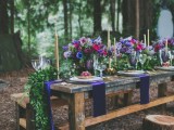 a bold woodland wedding tablescape with jewel toned blooms, a greenery runner and purple napkins
