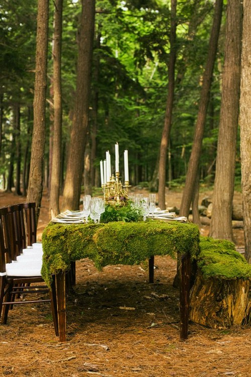 a woodland weddint table setting with a moss tablecloth, a greenery runner with white candles and simple plates