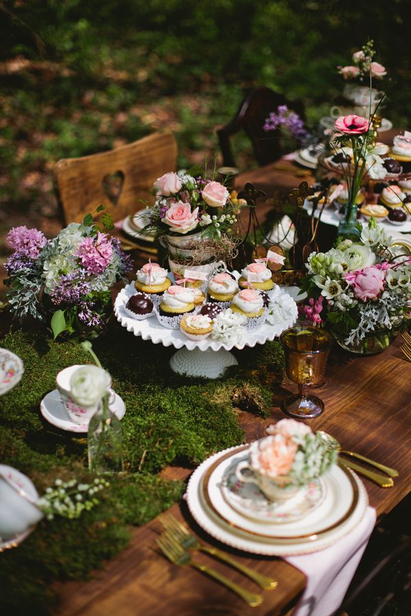 A woodland wedding tablescape with a moss tablecloth, some purple and pink romantic florals, gold cutlery and amber glasses