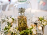 a glam woodland wedding centerpiece with moss, wood slices, blooms, a tree stump with a succulent in a cloche