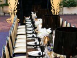 a refined black, gold and white wedding tablescape with black lamps, gold vases with white blooms and black glasses