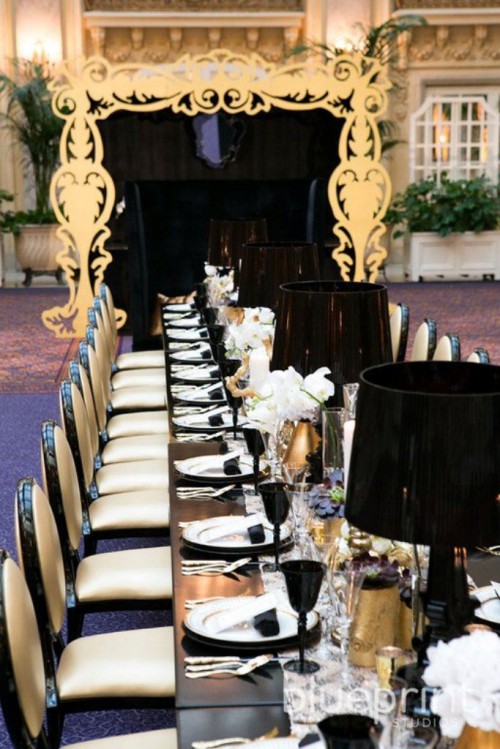 a refined black, gold and white wedding tablescape with black lamps, gold vases with white blooms and black glasses