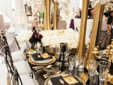 a black and gold wedding tablescape with tall gold vases, black and gold settings and white rose centerpieces