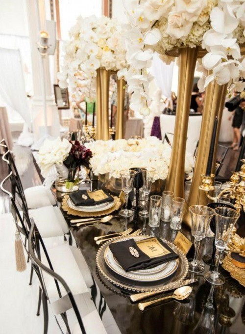 a black and gold wedding tablescape with tall gold vases, black and gold settings and white rose centerpieces