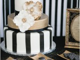 a gold and striped black and white wedding cake with sugar blooms