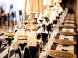 a striped black and white tablecloth, black glasses and candle holders, white bloom centerpieces