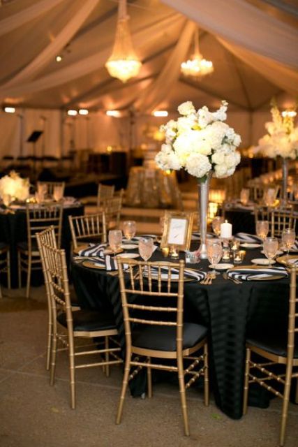 a black, white and gold wedding tablescape with striped napkins, a lush white bloom centerpiece, white candles and a gold frame