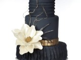 a textural black and gold wedding cake topped with a white sugar bloom