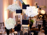 black and white floral centerpieces, a black and gold table number, black glasses and gold chargers