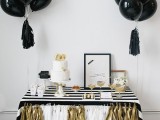 a black, white and gold wedding dessert table with balloons and tassels, with a striped tablecloth and tasssel garlands