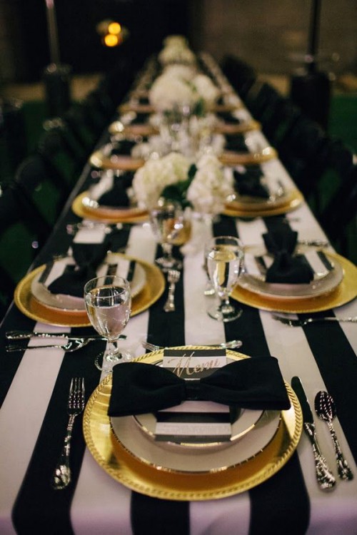 a chic tablescape with a striped tablecloth, black chargers and cutlery, striped menus and black bows