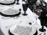 a modern black and white wedding table setting with a black lace table runner, black glasses, black and white plates and silver touches