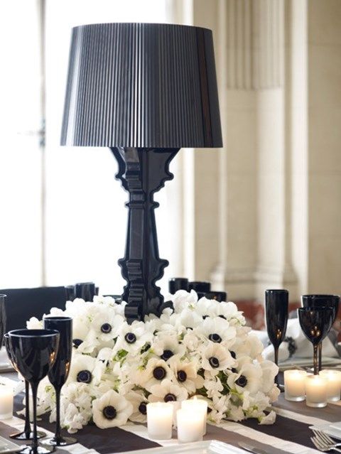 a black and white tablescape with a floral centerpiece and a black lamp, black glasses, white candles and black napkins