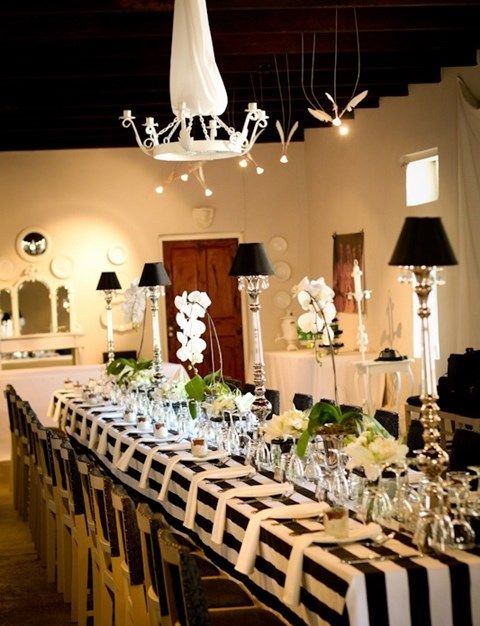 a stylish black and white tablescape with a striped tablecloth, black lamps, neutral blooms and glasses