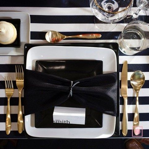 a chic place setting with a striped tablecloth, black napkins and plates and silver touches