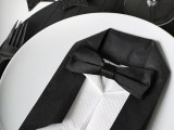 a simple black and white place setting with a tux folded napkin, ornaments and stars, a black charger and a white plate