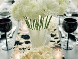a laconic black and white wedding tablescape with white blooms, a botanical table runner, black glasses