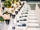 a contemporary black and white tablescape with a striped table runner, neutral blooms and greenery topiaries with lights, black glasses and napkins