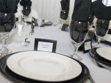 a minimalist black and white table setting with black chargers and napkins, black cards and all the rest done in white