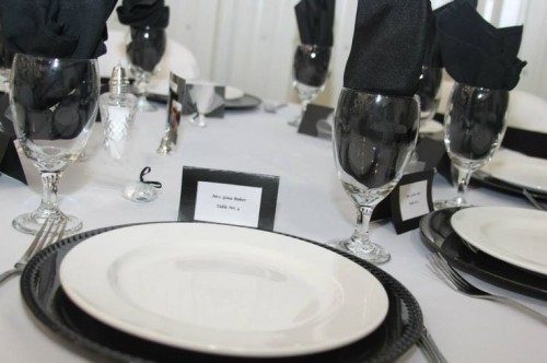 a minimalist black and white table setting with black chargers and napkins, black cards and all the rest done in white