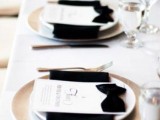 an elegant modern wedding tablescape with black napkins and bow menus, white chargers and clear glasses