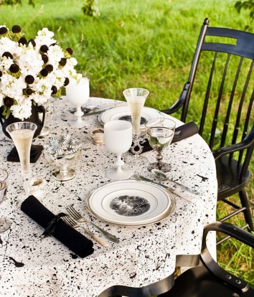 a black and white splatter tablecloth, a black and white floral centerpiece, black napkins and black and white plates