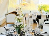 a chic black and white tablescape with a white tablecloth, black placemats, a white ochid and a refined chandelier over the table