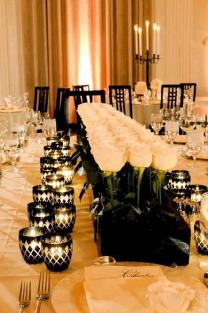 a gorgeous refined black and white tablescape with a large and long white rose centerpiece in a black box, black geometric candle holders and white porcelain