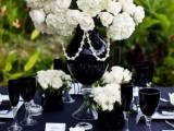 a refined black and white tablescape with a large white floral centerpiece and beads, black glasses, napkins and white porcelain