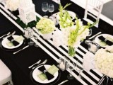 a modern tablescape with a black tablecloth, a striped black and white table runner, neutral blooms and black chargers and napkins