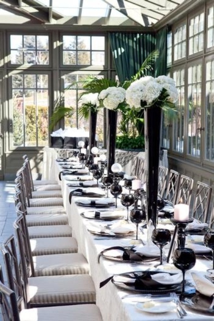 an exquisite black and white tablescape with black plates and glasses, tall black vases and white blooms, white candles in black candle holders