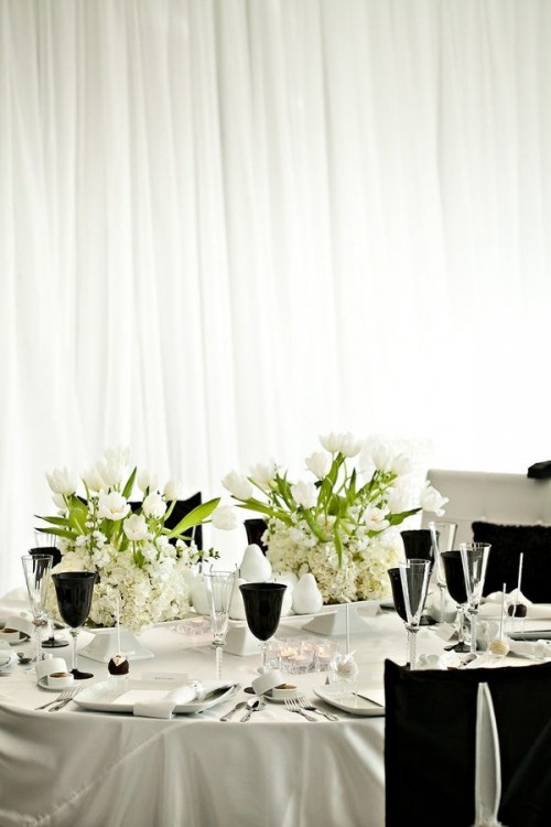 a chic tablescape with white floral centerpieces, black glasses, neutral porcelain and black chair covers
