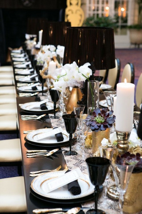 a black and white tablescape with black napkins, black glasses and lamps, a printed table runner and white pillar candles