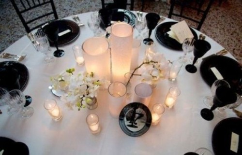 a white tablecloth, a large centerpiece of tall candleholders and white blooms, black glasses and black chargers