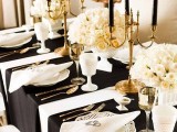 a refined table settign with a white tablecloth, black napkins, white rose centerpieces, black candles and gold touches
