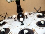 a chic black and white wedding tablescape with black chargers, a black vase with lush blooms, white candles and silver cutlery