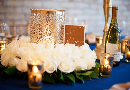 a navy, white and gold wedding table setting with lush blooms, candle holders and bottles