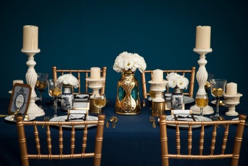 a navy, gold and white wedding tablescape with candles and lush white bloom centerpieces