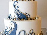 a white wedding cake decorated with gold and navy patterns and edible beads