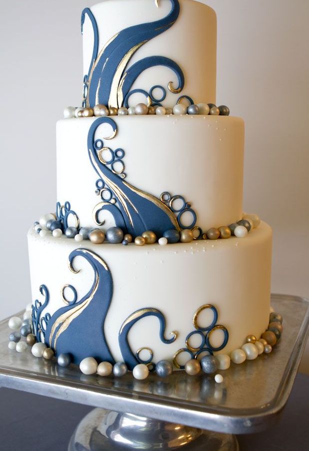 A white wedding cake decorated with gold and navy patterns and edible beads